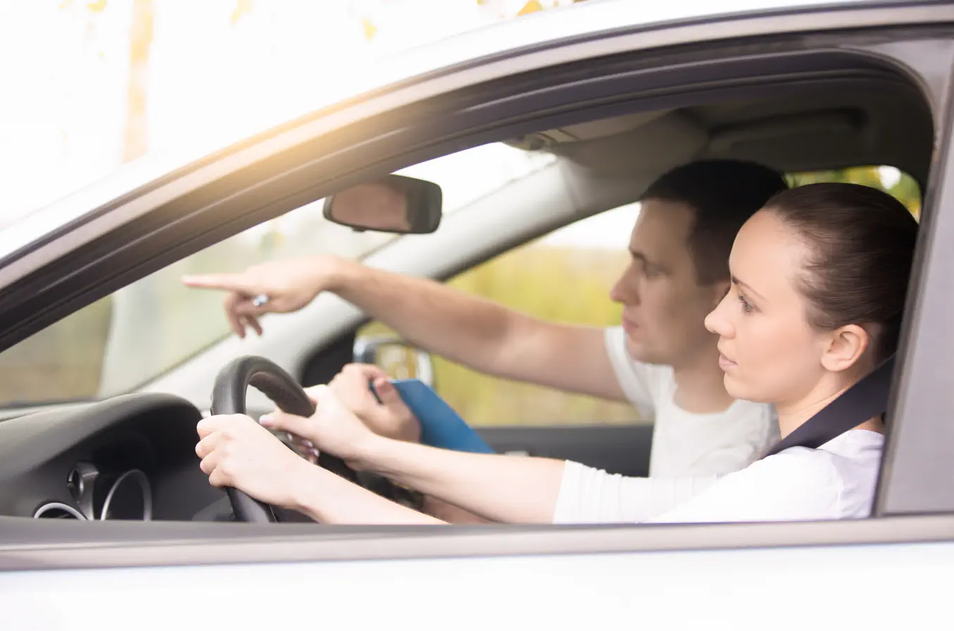 A student driver and instructor during driving lessons in Shelton, seen through the car window.